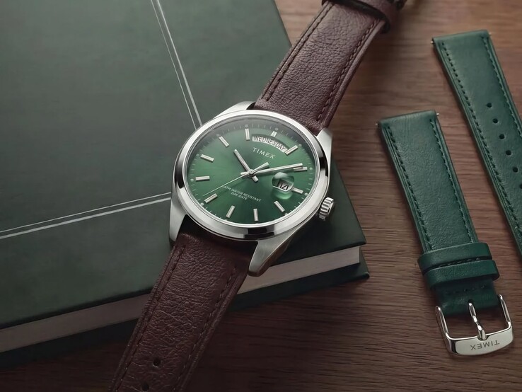De Timex Legacy Day and Date met zijn groene wijzerplaat en bruine leren band, weergegeven op een donkergroen boek naast de verwisselbare groene leren band.