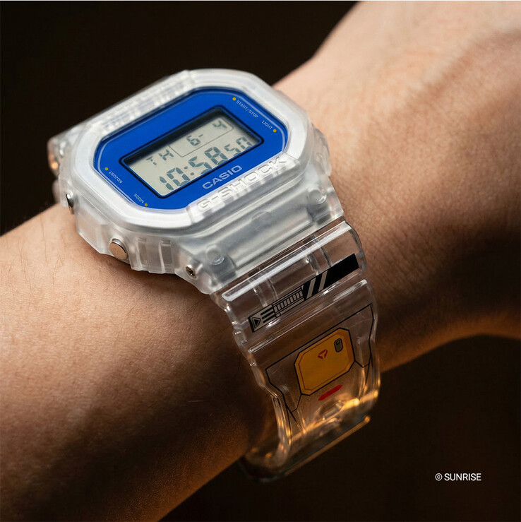 Casio G-Shock x Mobile Suit Gundam DW-5600GM26-7DR om de pols gedragen, met een kast en band van transparant hars, blauwe rand en op Gundam geïnspireerde afbeeldingen op de band.
