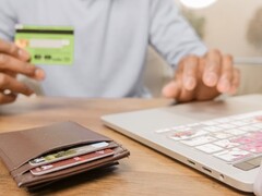 Persoon die een bankpas voor een laptop houdt, met een portemonnee op het bureau