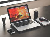MacBook Pro op een donker bureau naast een smartphone, een bril en een notitieboekje.