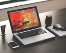 MacBook Pro op een donker bureau naast een smartphone, een bril en een notitieboekje.