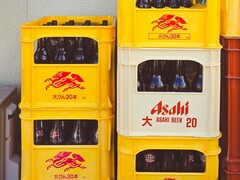 Gestapelde gele en witte plastic kratten gevuld met Asahi-bierflesjes, met Japanse tekst en rode logo&#039;s. (Afbeeldingsbron: Foto door Alazne Lazcano via Pexels)