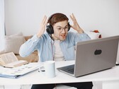 Man met een koptelefoon die gefrustreerd zijn handen opheft voor een laptop