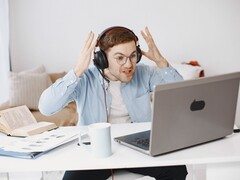 Man met een koptelefoon die gefrustreerd zijn handen opheft voor een laptop
