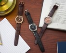 Drie Citizen Rolan-horloges, neergelegd op een houten bureau naast een notitieboekje, een pen, een lamp en een open boek, waaronder het model AW2110-14Z met zalmkleurige wijzerplaat.