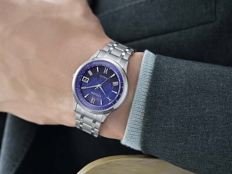 De Citizen Exceed CB1140-79L gedragen om de pols, met zijn blauwe wijzerplaat, zilverkleurige kast en geïntegreerde titanium schakelband tegen een donker jasje.