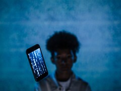 Zwevende smartphone met code op het scherm tegen een blauwe achtergrond, met een onscherpe persoon erachter