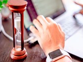 Een zandloper naast een hand op het toetsenbord van een laptop