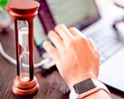 Een zandloper naast een hand op het toetsenbord van een laptop