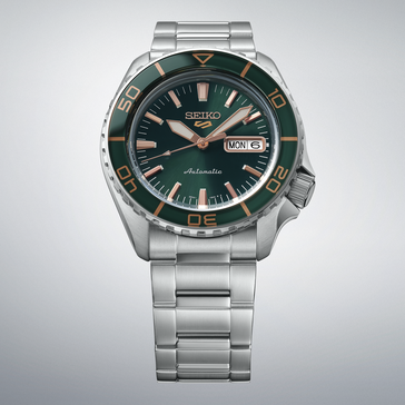 Seiko 5 Sports SKX HDB005 met een donkergroene wijzerplaat, bijpassende groene lunette, roségoudkleurige wijzers en indexen, en een roestvrijstalen horlogeband, weergegeven tegen een lichtgrijze achtergrond.