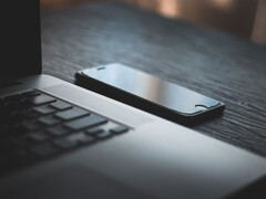 Een smartphone die naast een geopende laptop op een donker bureau ligt