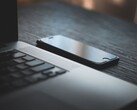 Een smartphone die naast een geopende laptop op een donker bureau ligt