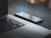 Een smartphone die naast een geopende laptop op een donker bureau ligt
