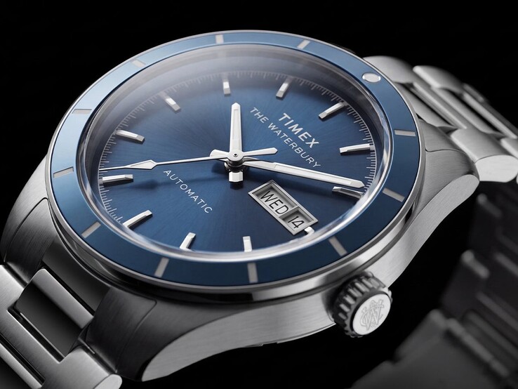 Close-up van de Timex Waterbury Heritage Automatic met blauwe wijzerplaat, waarop de lichtgevende wijzers, de aangebrachte uurmarkeringen en de dag- en datumweergave te zien zijn.