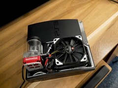 Aangepaste watergekoelde PlayStation 3 met een rode SysCooling-pomp en grote zwarte ventilator in de behuizing, geplaatst op een houten bureau. (Afbeelding bron: Zac Builds via YouTube)