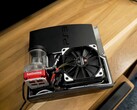 Aangepaste watergekoelde PlayStation 3 met een rode SysCooling-pomp en grote zwarte ventilator in de behuizing, geplaatst op een houten bureau. (Afbeelding bron: Zac Builds via YouTube)