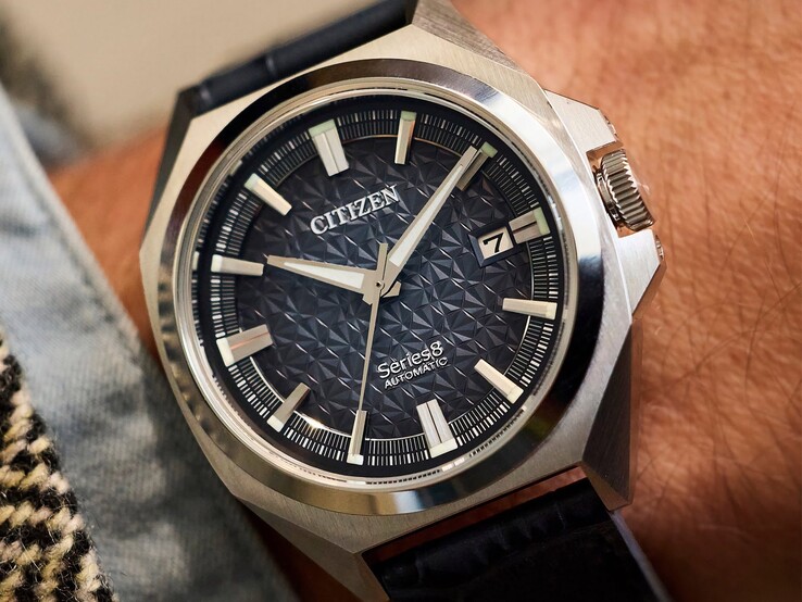 Een automatisch Citizen Series 8 831-horloge met een geometrische wijzerplaat in gebrand oranje en bruin, een goudkleurige kast en lunette, en een geïntegreerde goudkleurige H-link-armband, gedragen om de pols.