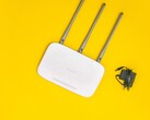 Witte wifi-router met drie antennes en een voedingsadapter op een gele achtergrond