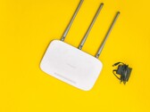 Witte wifi-router met drie antennes en een voedingsadapter op een gele achtergrond