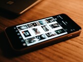 Een smartphone die op een houten bureau ligt, met op het scherm een raster van foto’s
