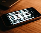 Een smartphone die op een houten bureau ligt, met op het scherm een raster van foto’s