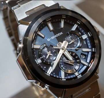 Close-up van de Casio G-Shock GST-W1000AD-2A met blauwe wijzerplaat, waarop de gelaagde indeling met drie subwijzerplaten, de lichtgevende markeringen, de zilveren wijzers en de zwarte lunette te zien zijn.