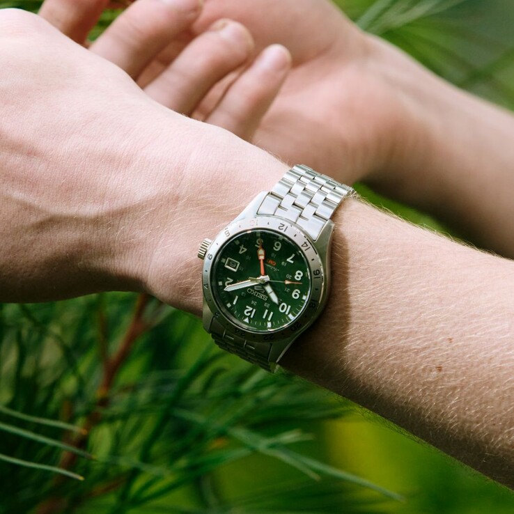 Vooraanzicht van de Seiko 5 Sports Field GMT HDB001 met een groene wijzerplaat, een vaste roestvrijstalen 24-uursring, een oranje GMT-wijzer en een stalen armband met vijf schakels.