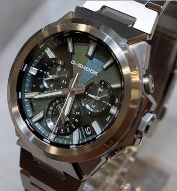Close-up van de Casio G-Shock GST-W1000D-3A met groene wijzerplaat, waarop de geometrisch gestructureerde wijzerplaat, de drie subwijzerplaten, de lichtgevende markeringen en de gepolijste roestvrijstalen lunette te zien zijn.
