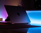 Een halfopen MacBook in een donkere kamer, waarbij licht door de opening op het bureau valt