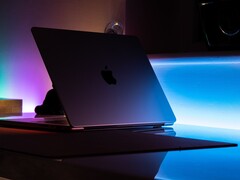 Een halfopen MacBook in een donkere kamer, waarbij licht door de opening op het bureau valt