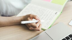 Iemand maakt aantekeningen in een notitieboekje naast een open laptop