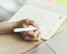 Iemand maakt aantekeningen in een notitieboekje naast een open laptop