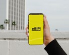 Een hand die een smartphone vasthoudt, met het woord „eSIM“ in grote letters op een geel scherm.