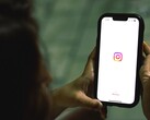 Vrouw die een smartphone met beide handen vasthoudt; op het scherm is het startscherm van Instagram te zien