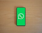 Een smartphone op een houten bureau waarop het groene startscherm van WhatsApp met het bijbehorende logo te zien is.