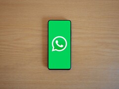 Een smartphone op een houten bureau waarop het groene startscherm van WhatsApp met het bijbehorende logo te zien is.