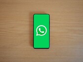 Een smartphone op een houten bureau waarop het groene startscherm van WhatsApp met het bijbehorende logo te zien is.